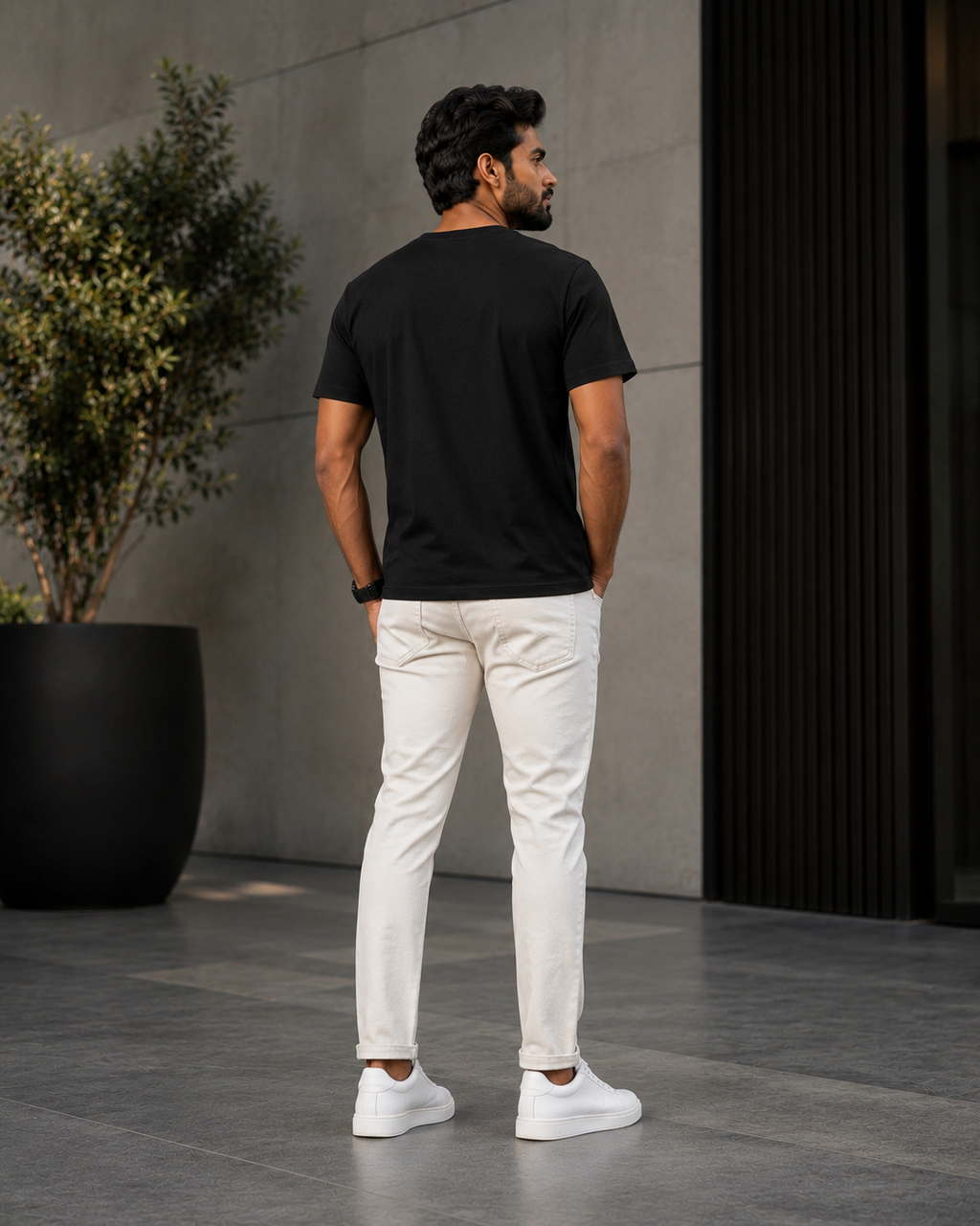 Back view of a model wearing a premium black t shirt for men with off-white jeans and white sneakers outdoors.