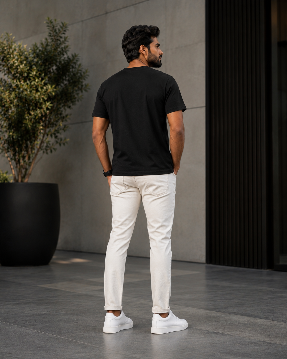 Back view of a model wearing a premium black t shirt for men with off-white jeans and white sneakers outdoors.