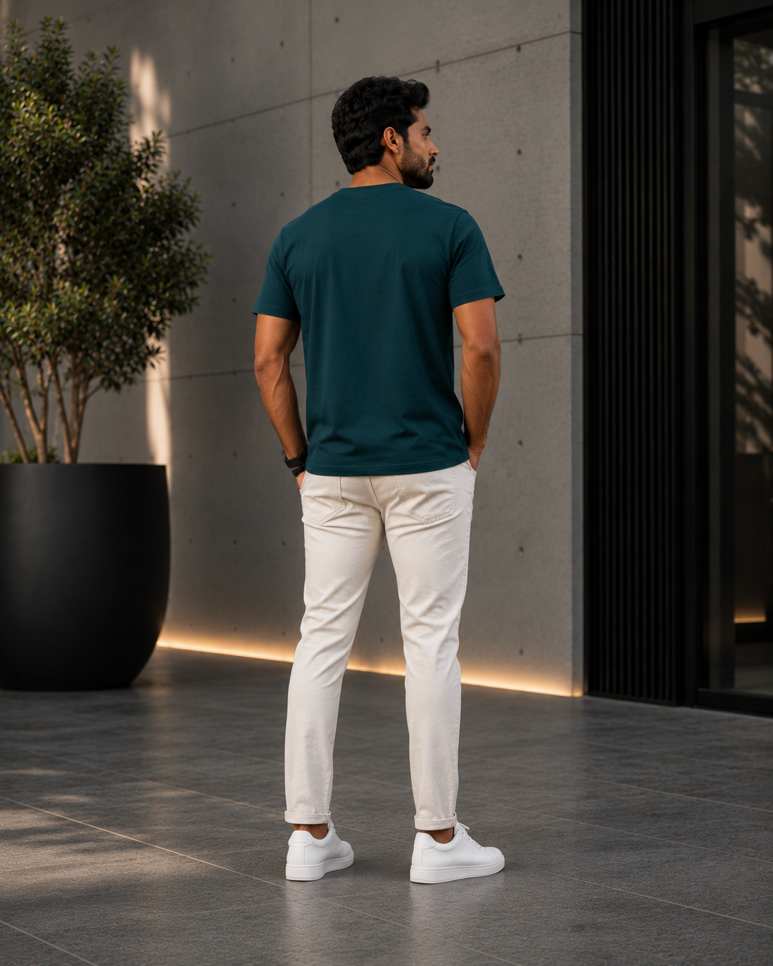 Back view of a model wearing a premium teal blue t shirt for men with off-white jeans and white sneakers outdoors.