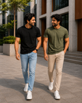 Two men walking outdoors in a modern urban setting wearing plain crew neck T-shirts for men, one in black with light blue jeans and the other in olive green with beige chinos paired with white sneakers for a casual everyday look.