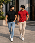 Two men walking outdoors wearing plain crew neck T-shirts for men, one in black with light blue jeans and the other in red tee with beige chinos paired with white sneakers for a casual everyday look.