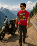 Kevin wearing a red graphic printed T-shirt for men with a RIDE CAMP EXPLORE REPEAT design, standing beside an adventure motorcycle on a scenic mountain road.
