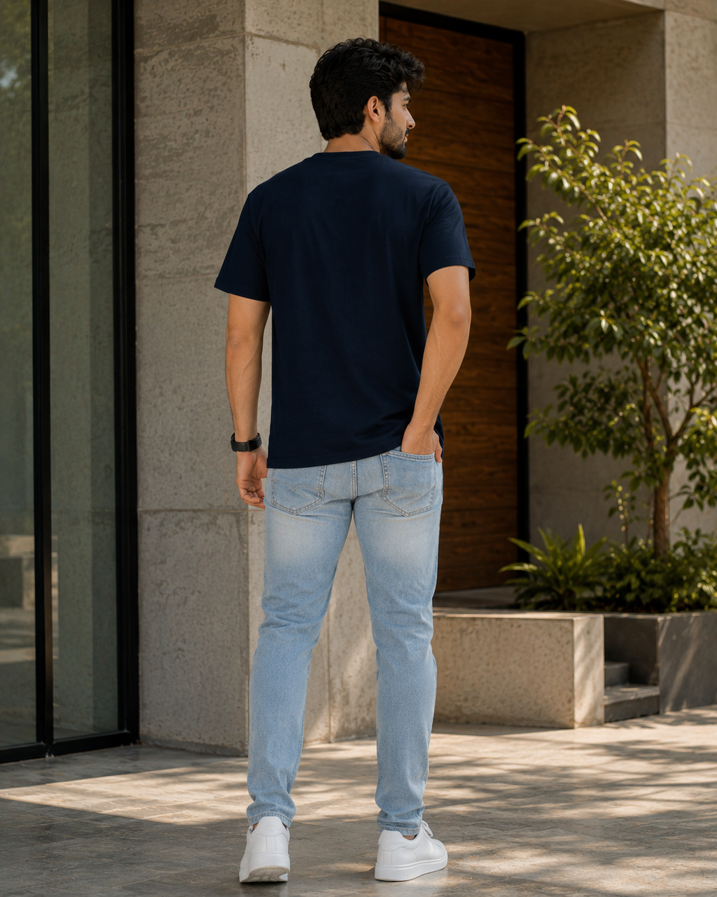 Back view of a model wearing Deadline Survivor graphic printed t shirt for men with light wash jeans outdoors.