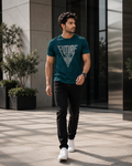 A man walking outdoors in a dark teal  blue graphic t-shirt with 'FUTURE IS NOW' printed in white, paired with black pants and white sneakers.