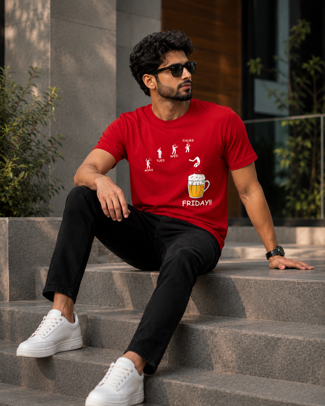 Model sitting on stone steps wearing Beer on Friday graphic printed t shirt for men with black pant and white sneakers.